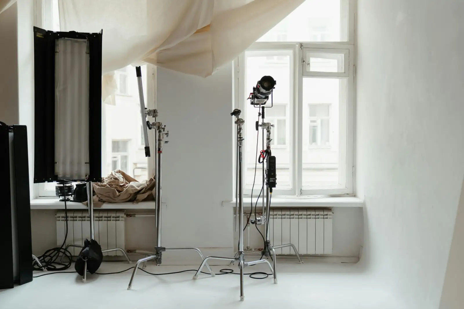 A white room with tall windows, lighting stands and a draped sheet