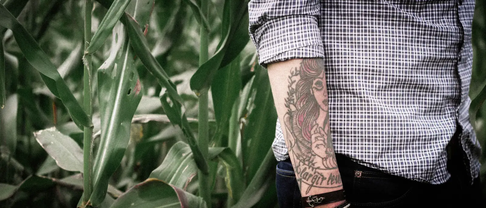 A tattoo of a woman’s portrait and a banner on a forearm, below a rolled-up plaid sleeve